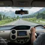 A view from inside a moving cab, showing the driver and the road ahead leading towards massive, lush green Himalayan mountains under a cloudy sky on the route from Pahalgam to Srinagar. A small digital map overlay confirms the destination.